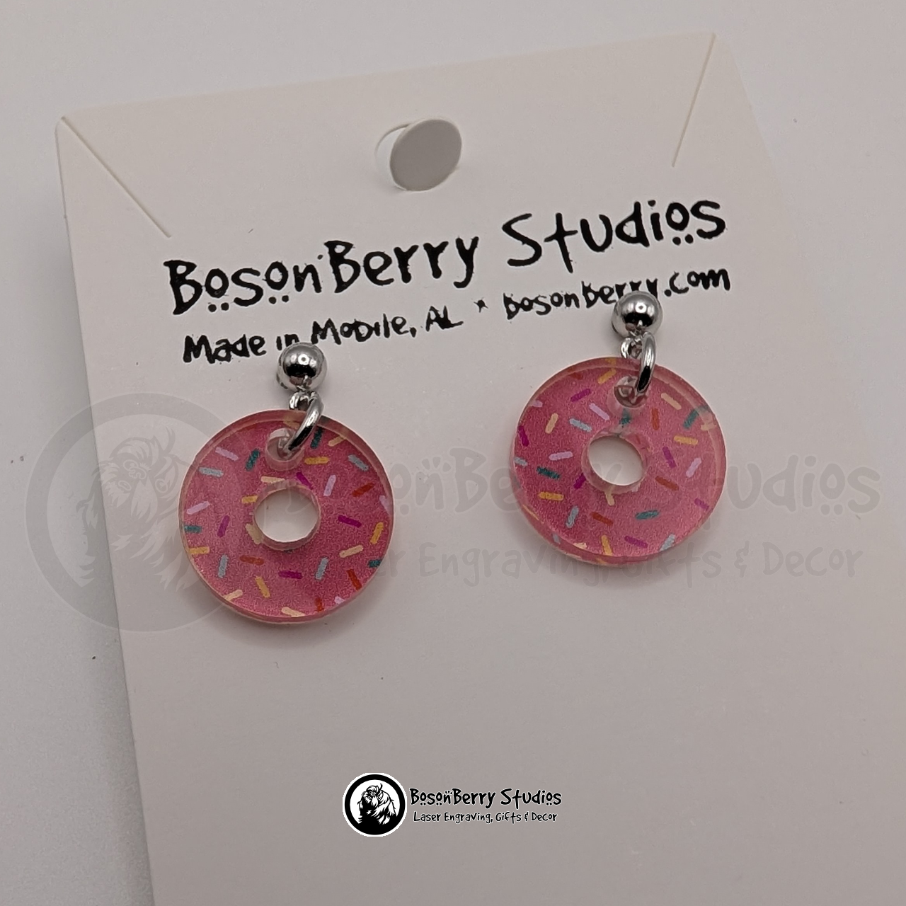 Tiny pink donut-shaped acrylic earrings, with a colorful sprinkle pattern, on a BosonBerry Studios card.