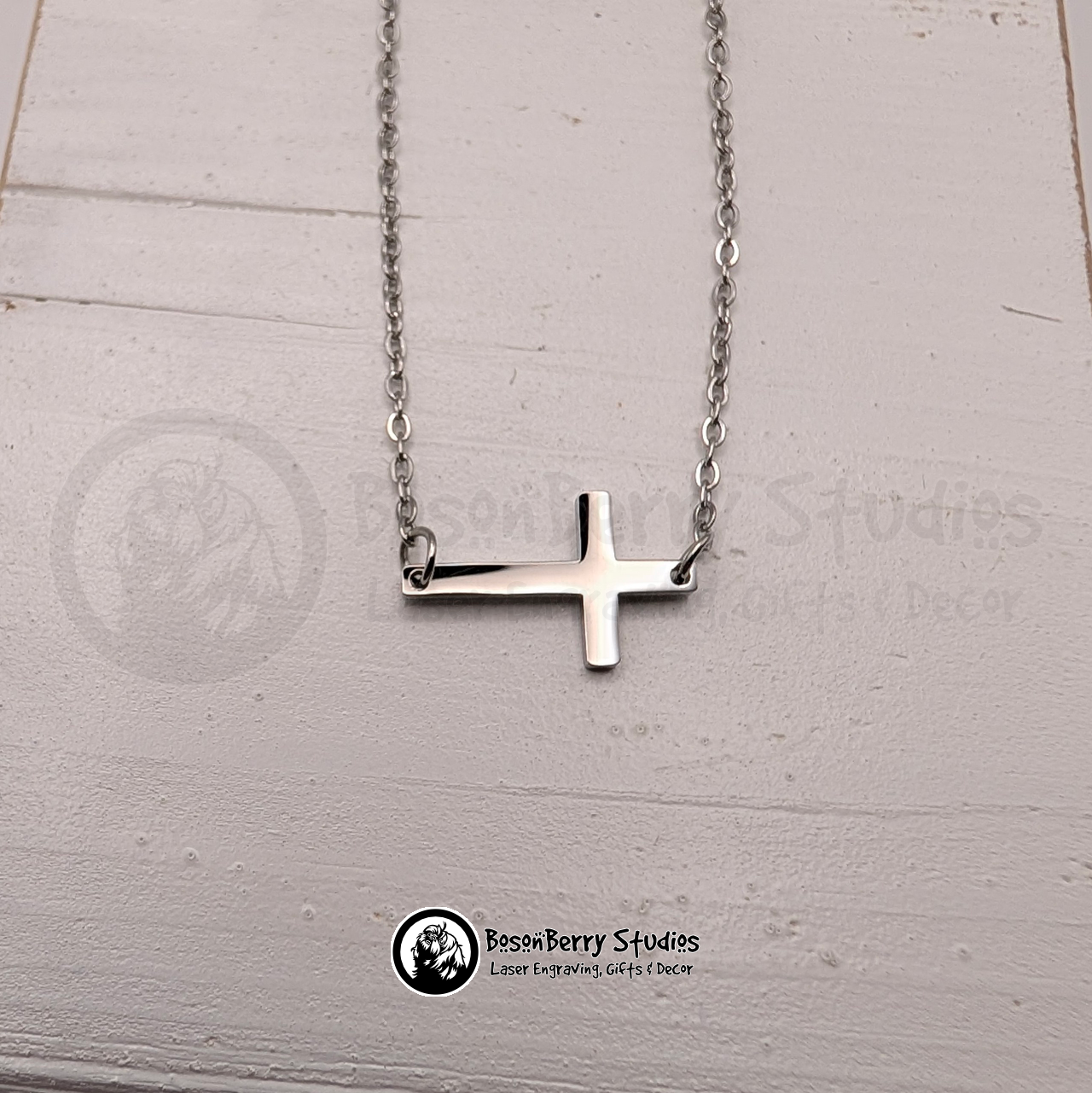 Silver tiny cross necklace on a white wooden stand with 'BosonBerry Studios' branding.