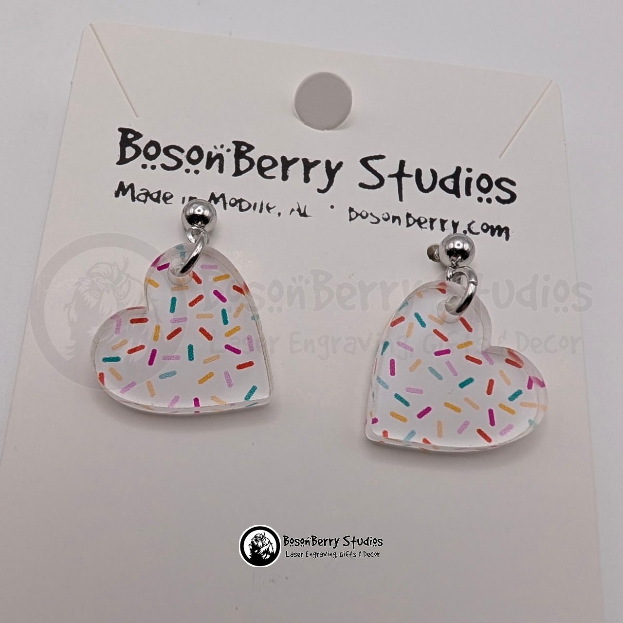 Tiny white heart-shaped acrylic earrings, with a colorful sprinkle pattern, on a BosonBerry Studios card.