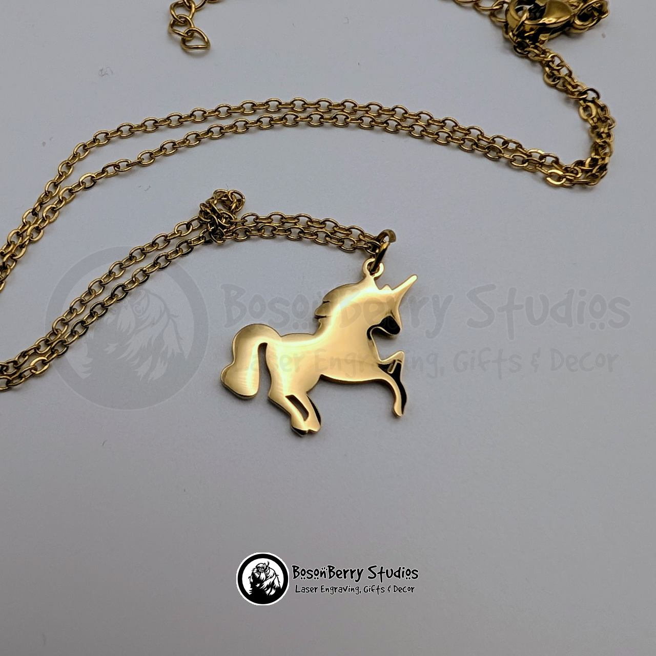 A gold necklace with a unicorn shaped pendant on a white background with 'BosonBerry Studios' branding.