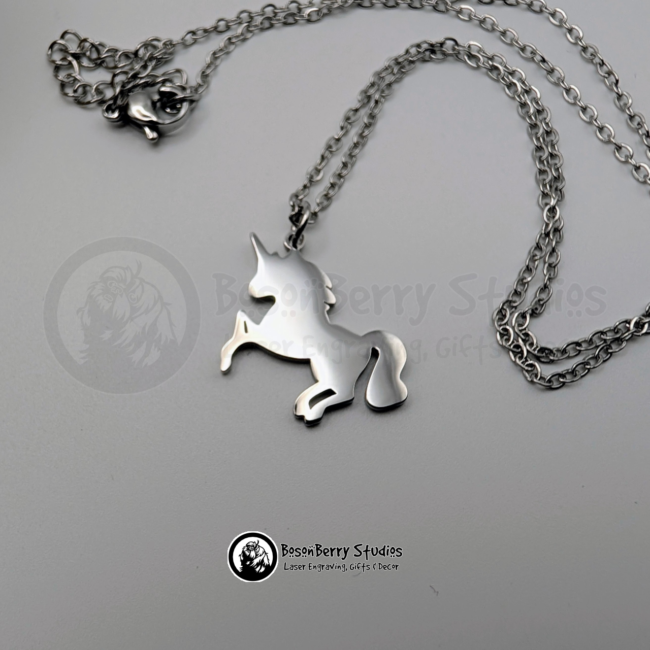 A silver necklace with a unicorn shaped pendant on a white background with 'BosonBerry Studios' branding.
