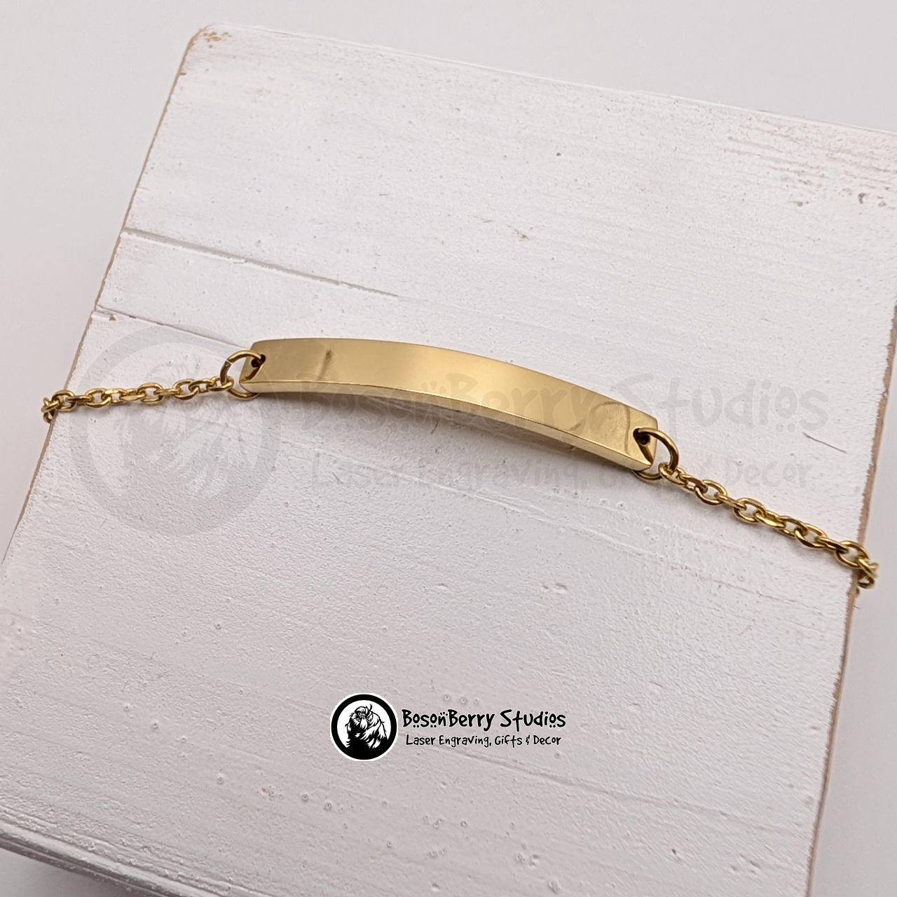 Gold bar bracelet on a white wooden stand with 'BosonBerry Studios' branding.