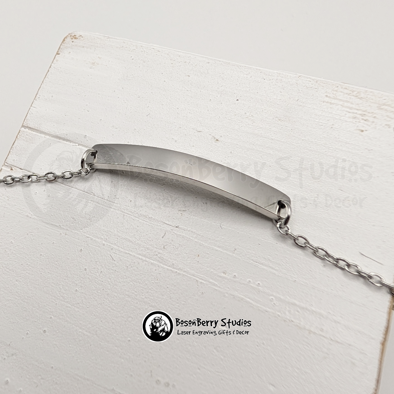 Silver bar bracelet on a white wooden stand with 'BosonBerry Studios' branding.