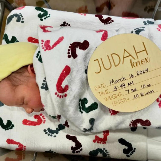 A newborn baby with a sign displaying his birth stats