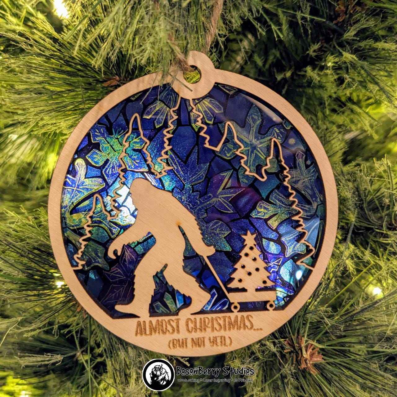 Almost Christmas (But Not Yeti) Ornament with Blue Snowflake transparent backer, hanging from Christmas tree